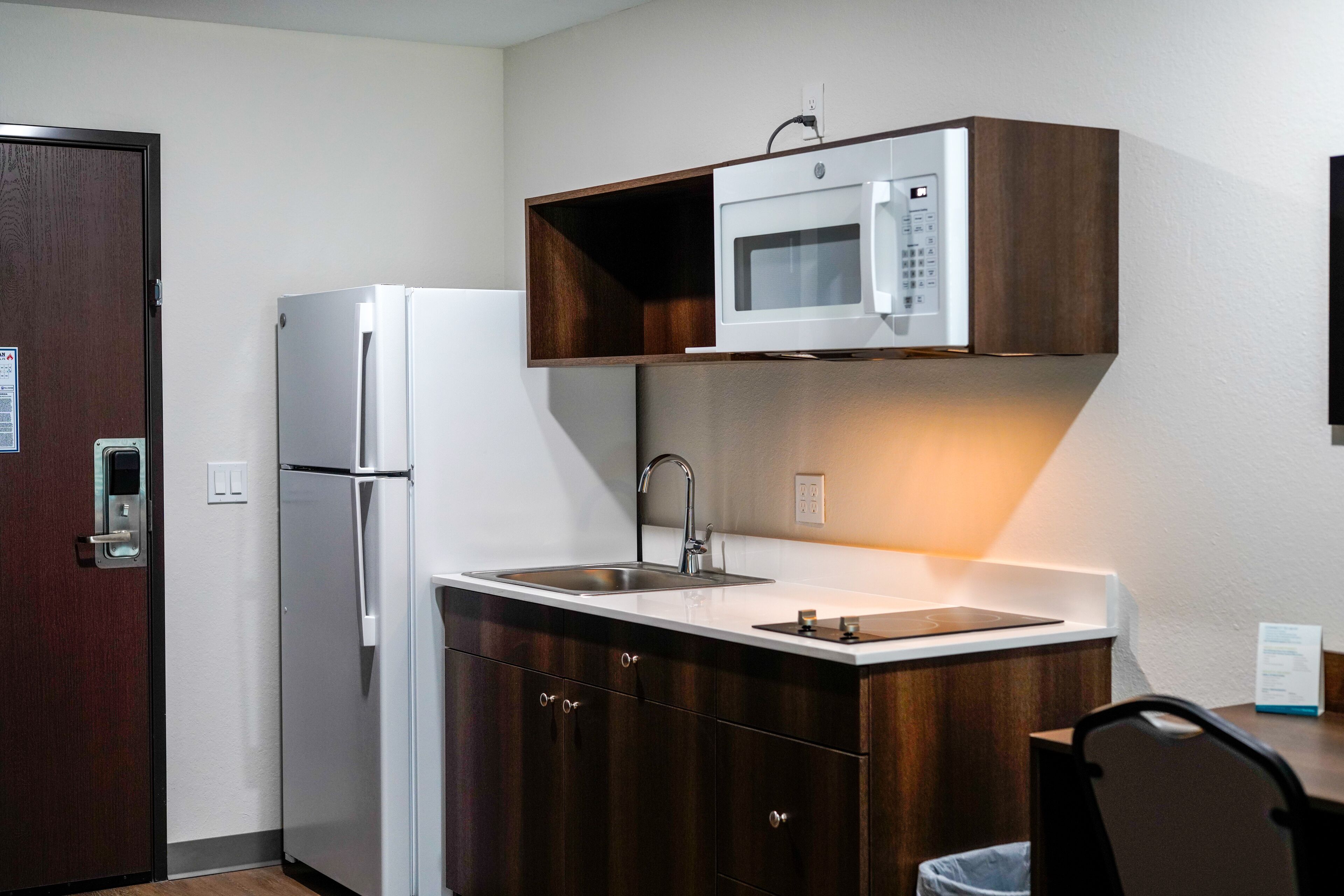 Una cocina compacta con microondas integrado, un lavamanos de acero inoxidable y un refrigerador.