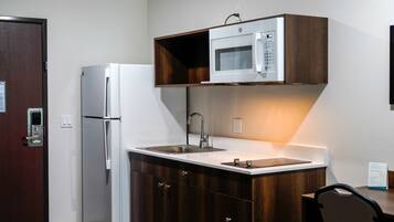 Una cocina compacta con microondas integrado, un lavamanos de acero inoxidable y un refrigerador.