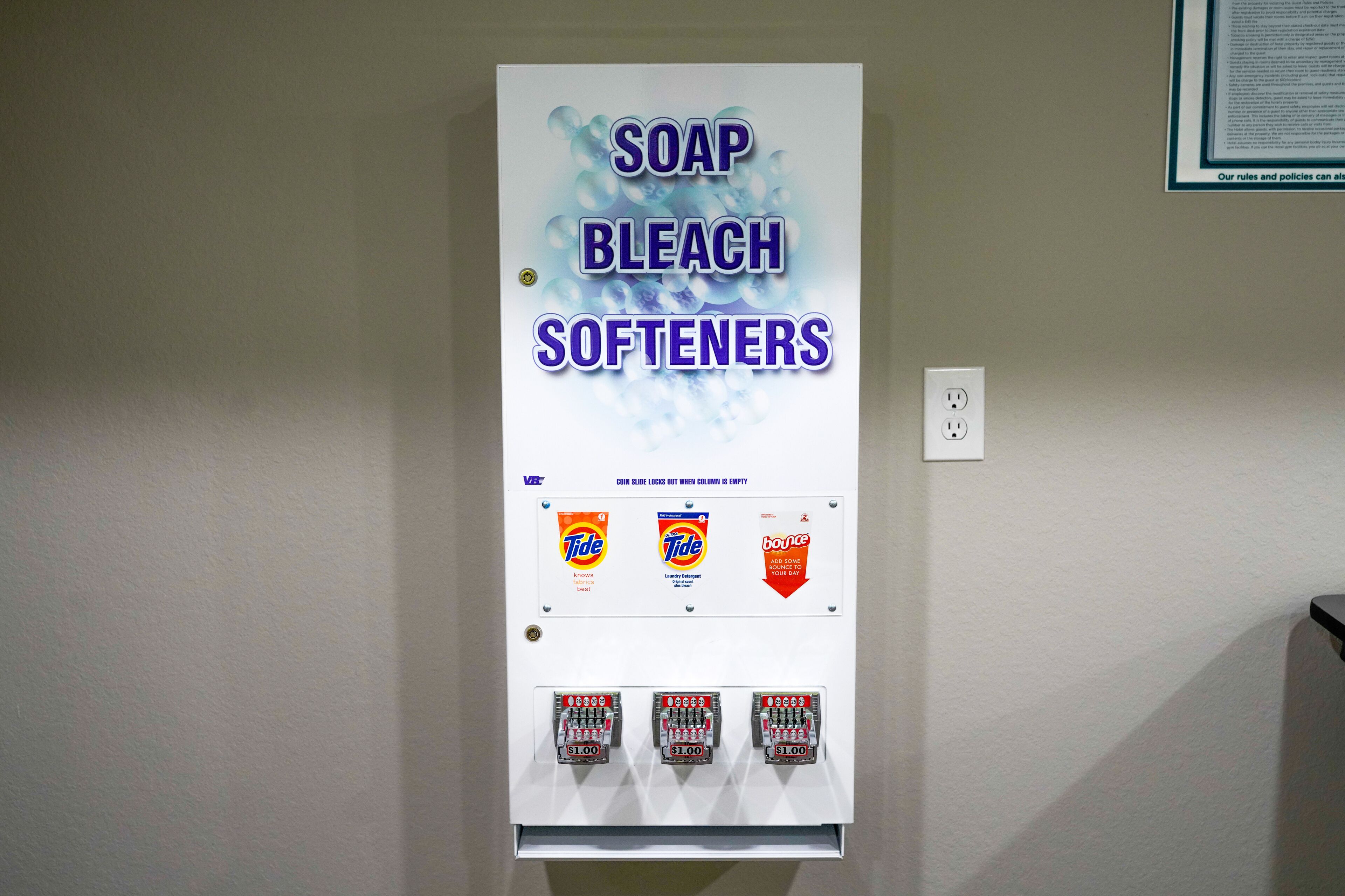 Un distributeur automatique portant l’inscription « SAVON, JAVEL, ADOUCISSANTS » et proposant des produits des marques Tide et Bounce.