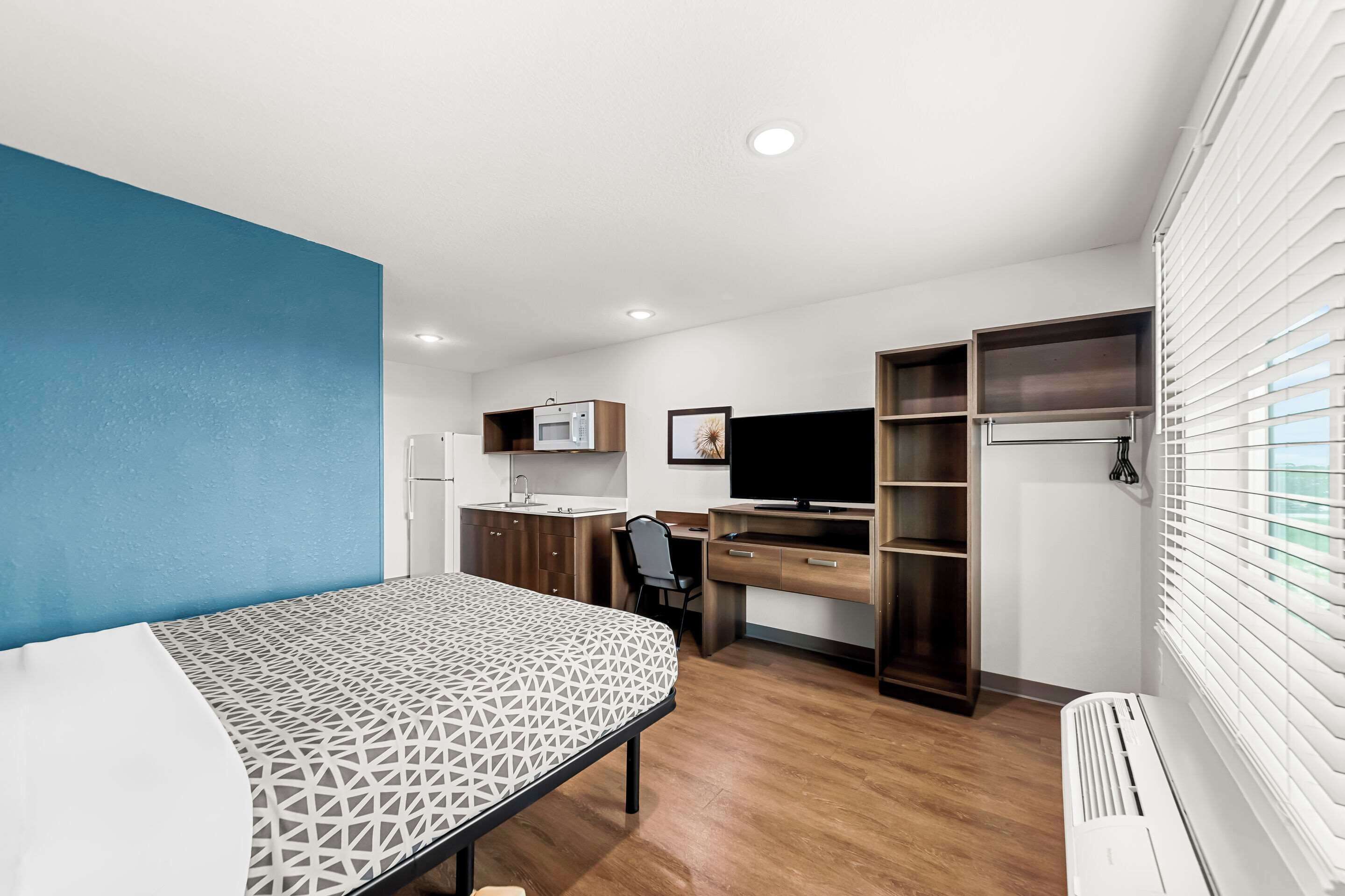 A compact bedroom with a bed, a desk, a chair, a TV, a wardrobe, and a radiator.