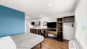 A compact bedroom with a bed, a desk, a chair, a TV, a wardrobe, and a radiator.