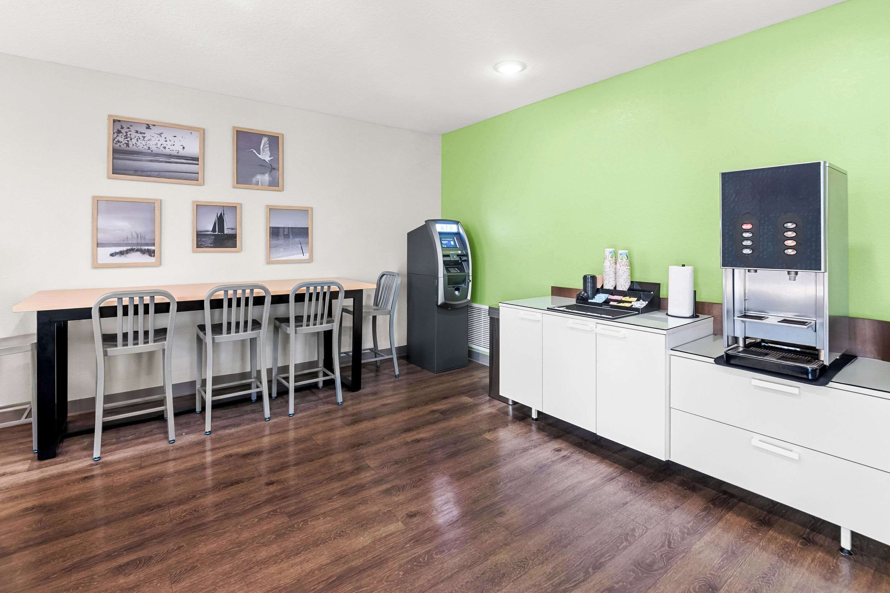 A modern kitchen with a wooden table, chairs, a coffee machine, and a refrigerator.