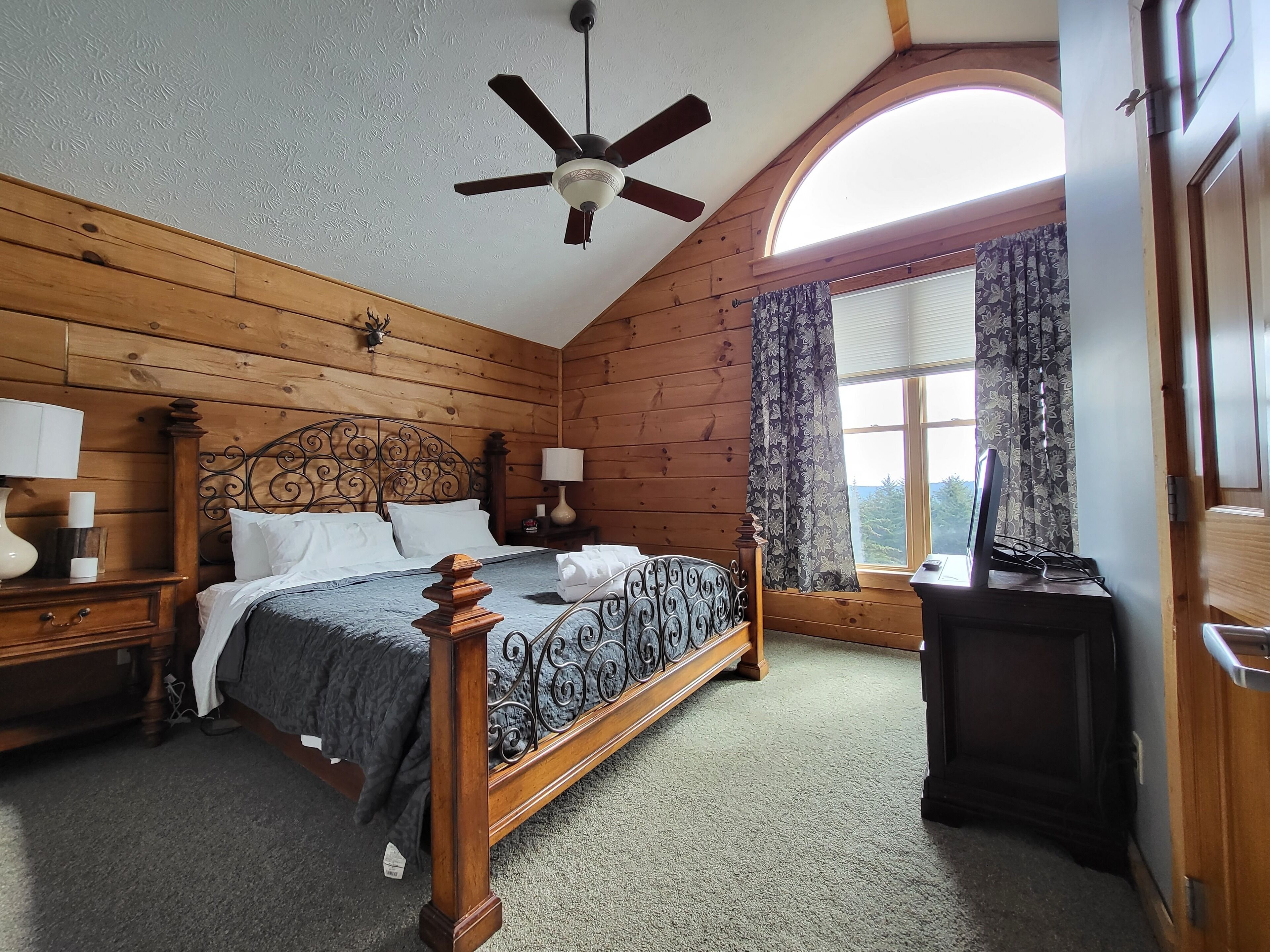 Une chambre aux murs lambrissés, dotée d’un lit à baldaquin, d’un ventilateur de plafond et d’une fenêtre avec des rideaux.