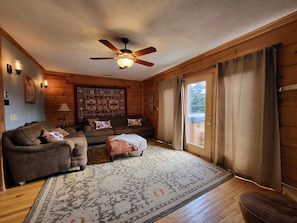 A cozy log cabin interior with a ceiling fan, a large rug, and a wooden floor.