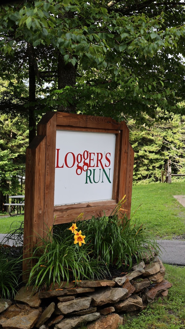 A wooden sign with the text "Loggers Run" surrounded by greenery and flowers.