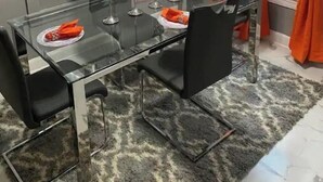Ein Essbereich mit einem Glastisch, schwarzen Stühlen und orangefarbenen Servietten.