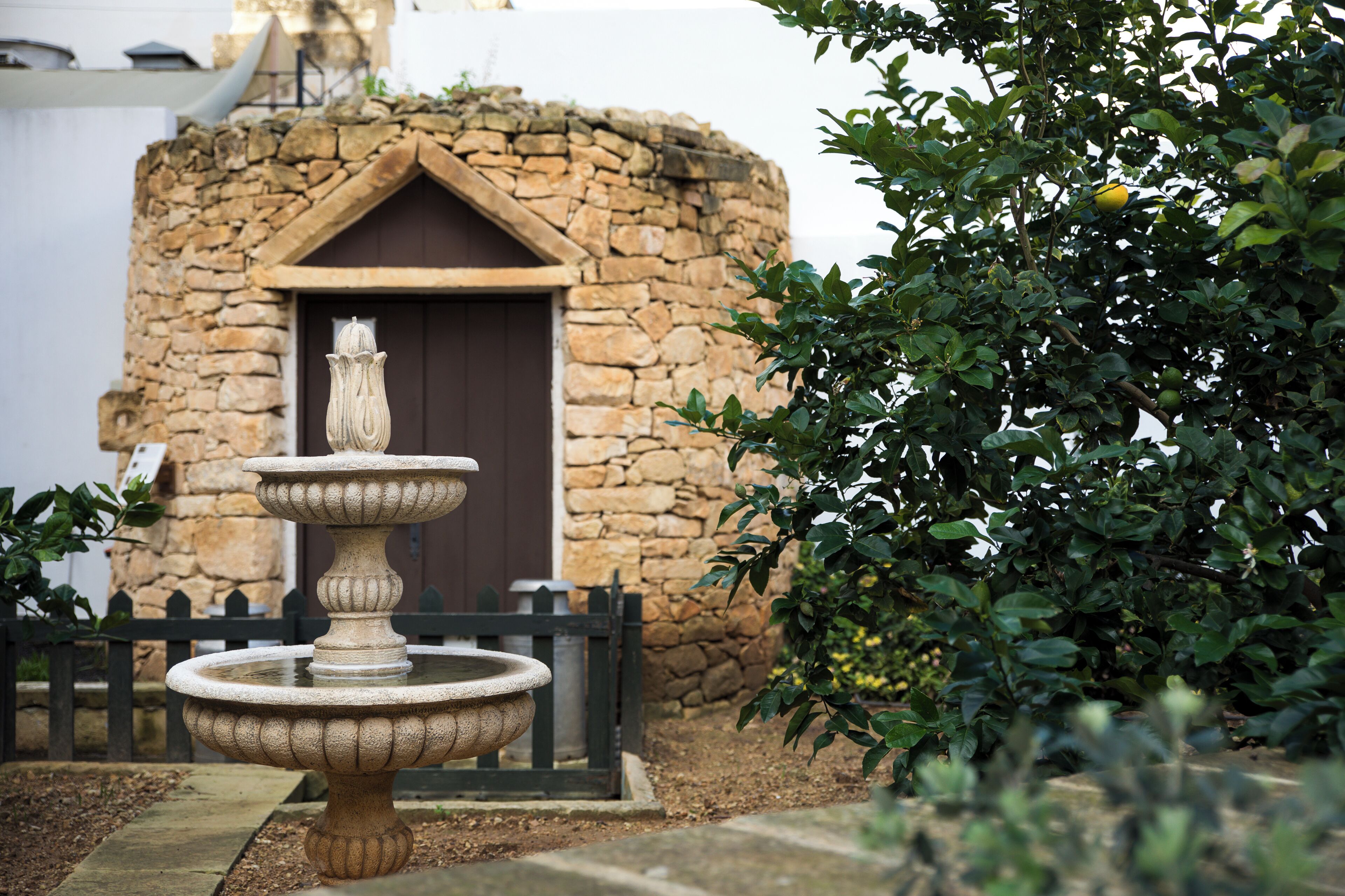 A stone fountain with a tiered design in front of a stone building with a dark brown door.