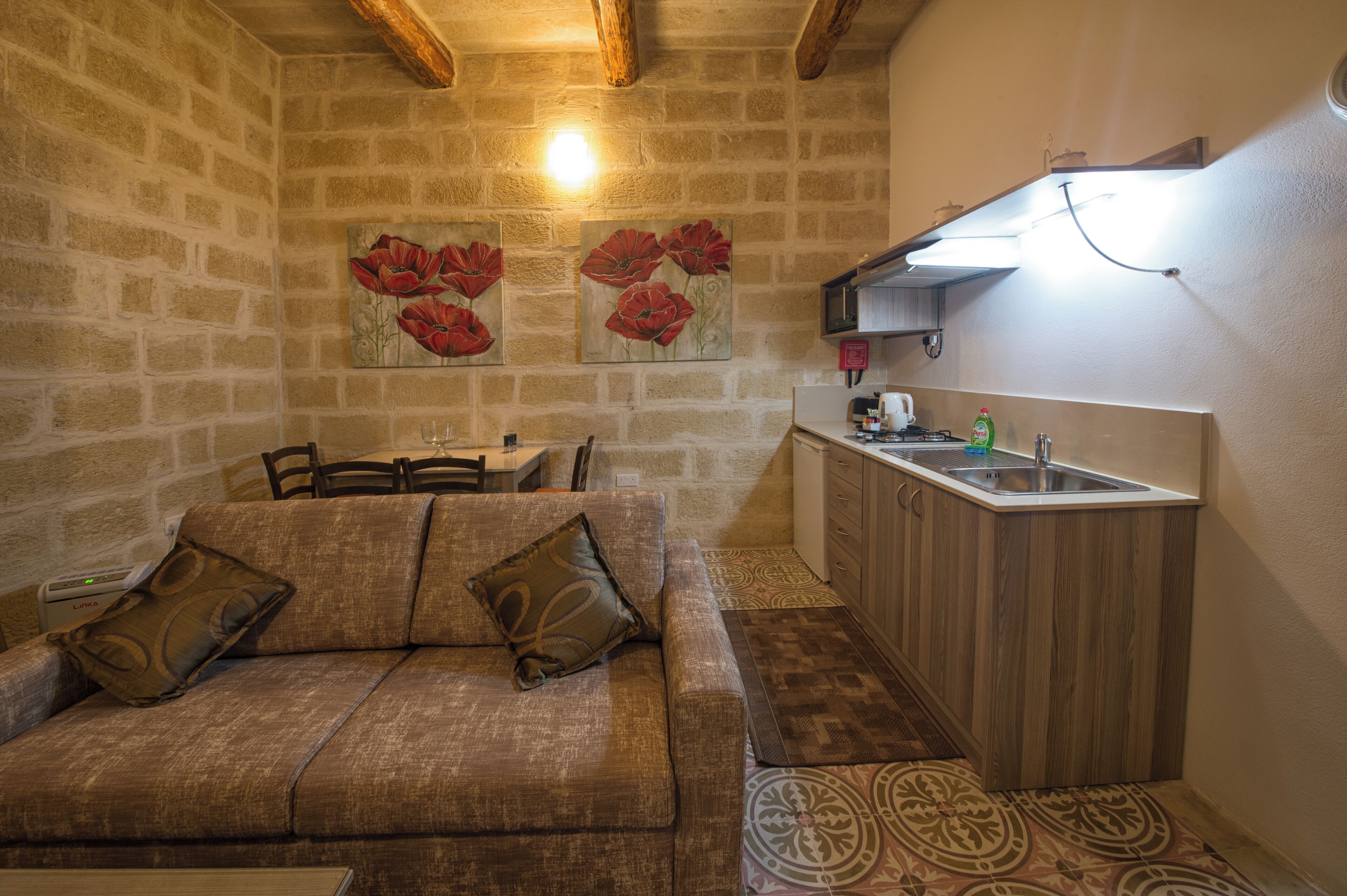 Une pièce chaleureuse comprenant un canapé, une table à manger et un coin cuisine avec un évier et des placards en bois.