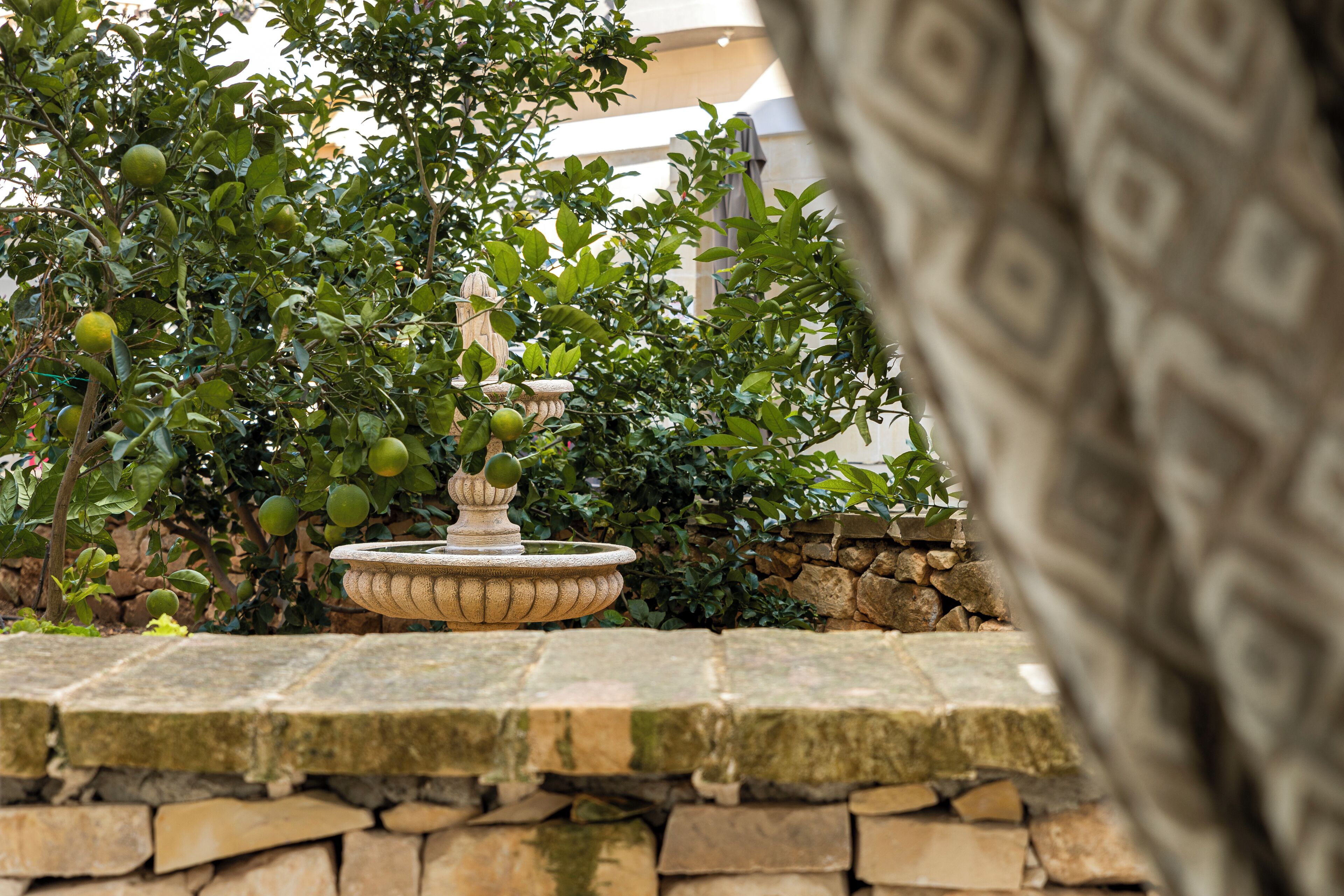 A stone fountain surrounded by lush greenery and a stone wall.
