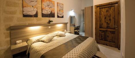 A bedroom with a wooden headboard, a bed with patterned bedding, a nightstand, a dresser, and a wooden door.
