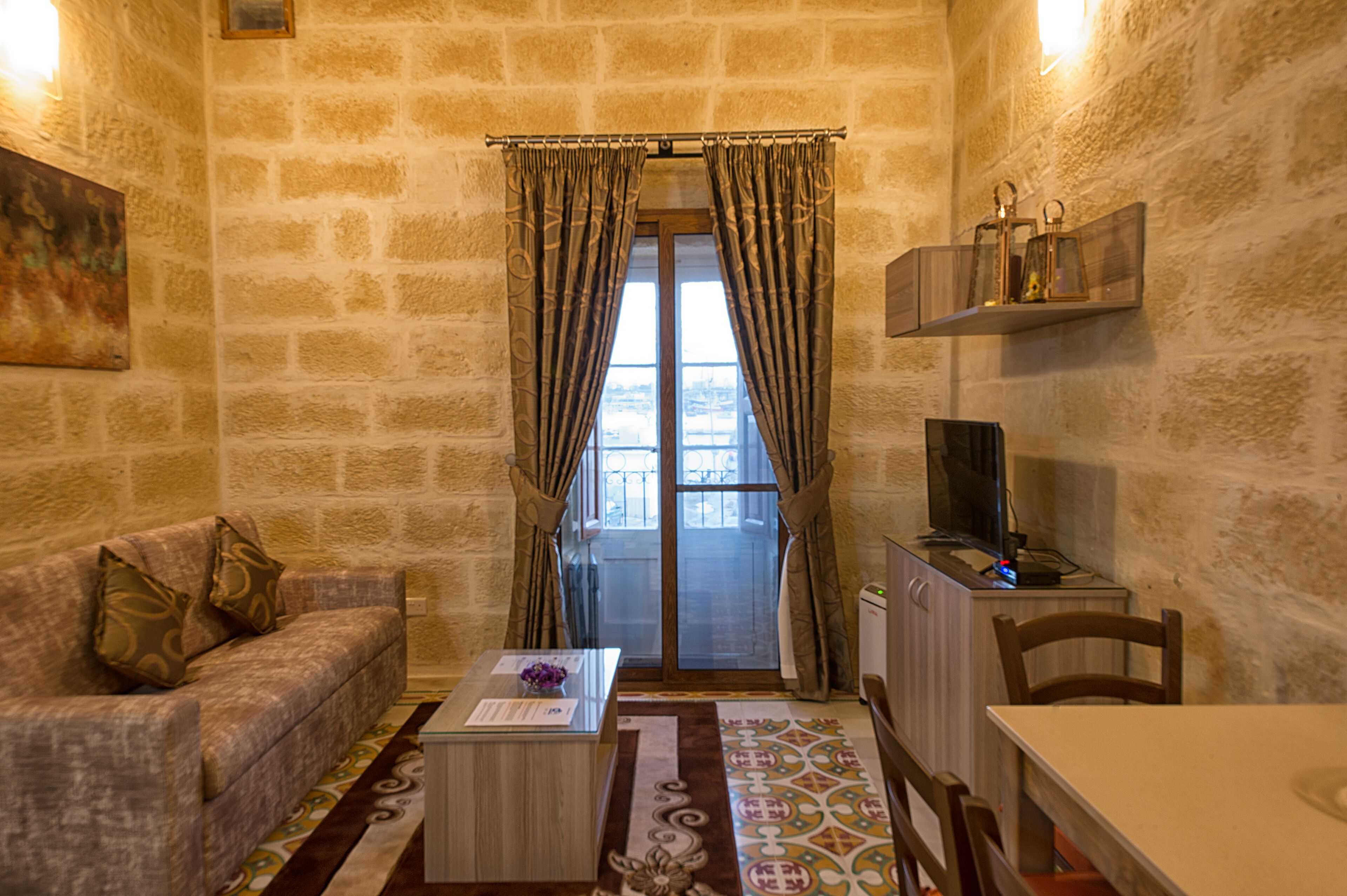 A cozy room with a stone wall, a sofa, a coffee table, a TV, and a window with curtains.