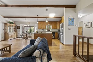 Un salón espacioso con un sofá grande, suelo de madera y una zona de cocina con armarios de madera y electrodomésticos modernos.