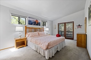 Quarto com cama grande, duas mesas de cabeceira com luminárias, um armário de madeira e uma porta de vidro deslizante para uma varanda.