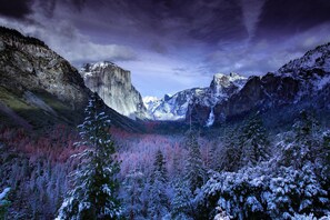 Paisagem montanhosa com árvores cobertas de neve e uma rocha imponente.