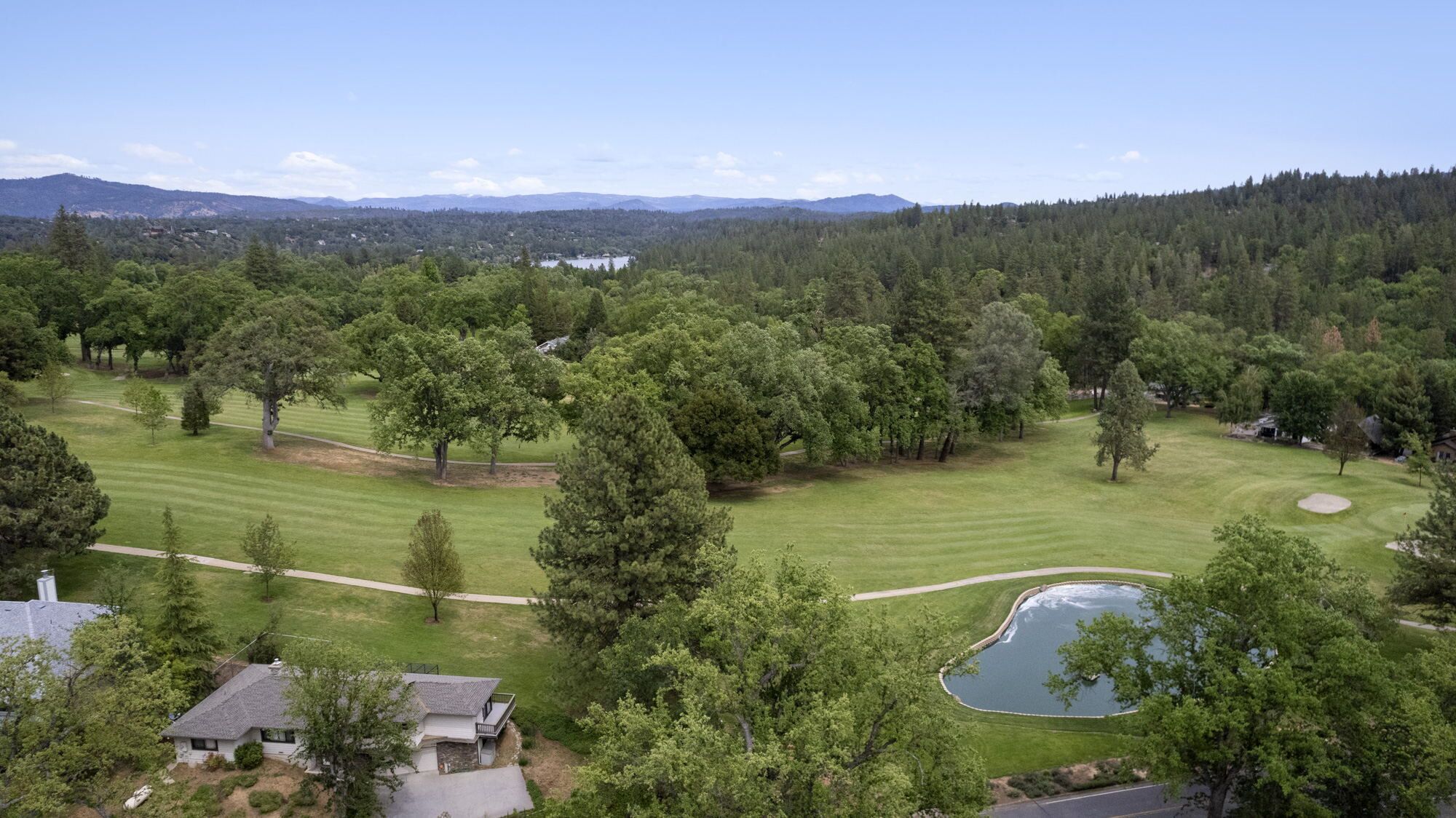 A golf course with a pond, surrounded by dense forest and distant mountains.
