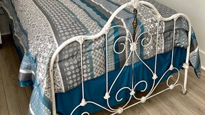Un lit bien fait, avec une couvre-lit à motifs et des oreillers, une tête de lit en métal blanche et un tableau accroché au mur.