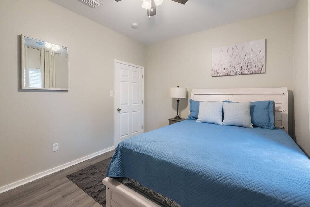 Un dormitorio con una cama, una mesita de noche, una lámpara, una puerta y un ventilador de techo.