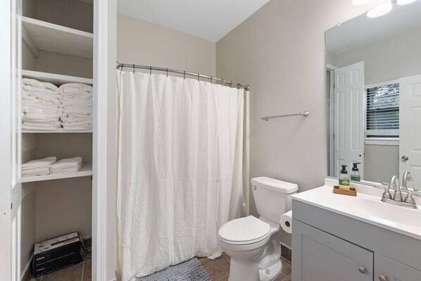 A bathroom with a toilet, a shower curtain, a sink with toiletries, and a mirror.