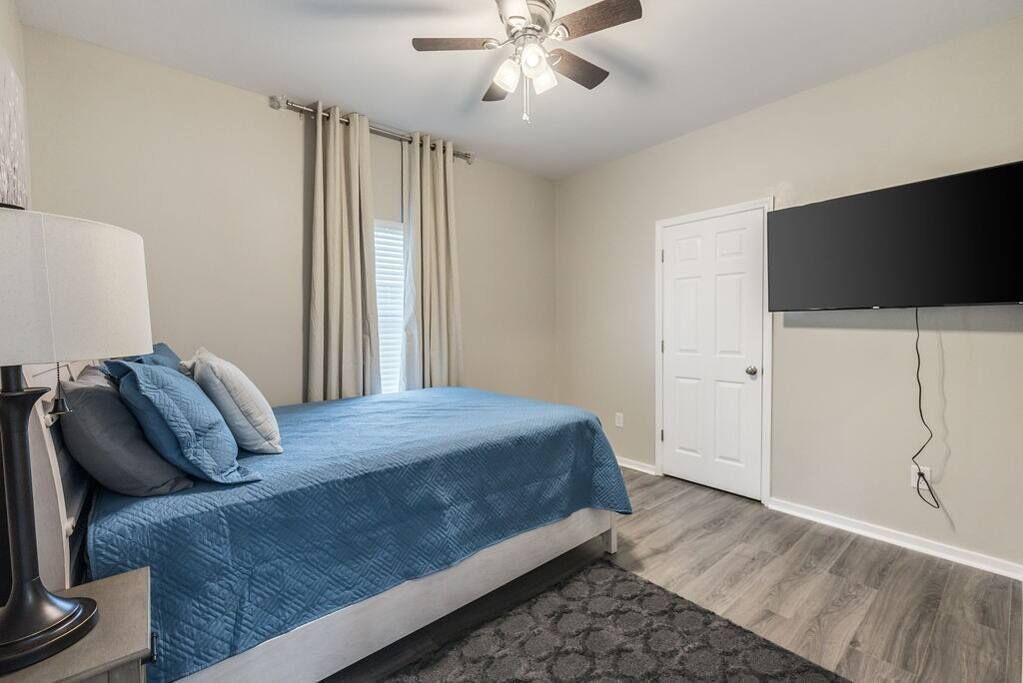 A bedroom with a bed, a ceiling fan, a TV mounted on the wall, and a door.