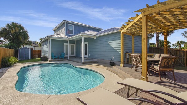 Un jardin avec une piscine, une pergola en bois illuminée et du mobilier d’extérieur.