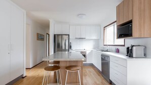 Una cocina moderna con armarios blancos, electrodomésticos de acero inoxidable y taburetes de madera.