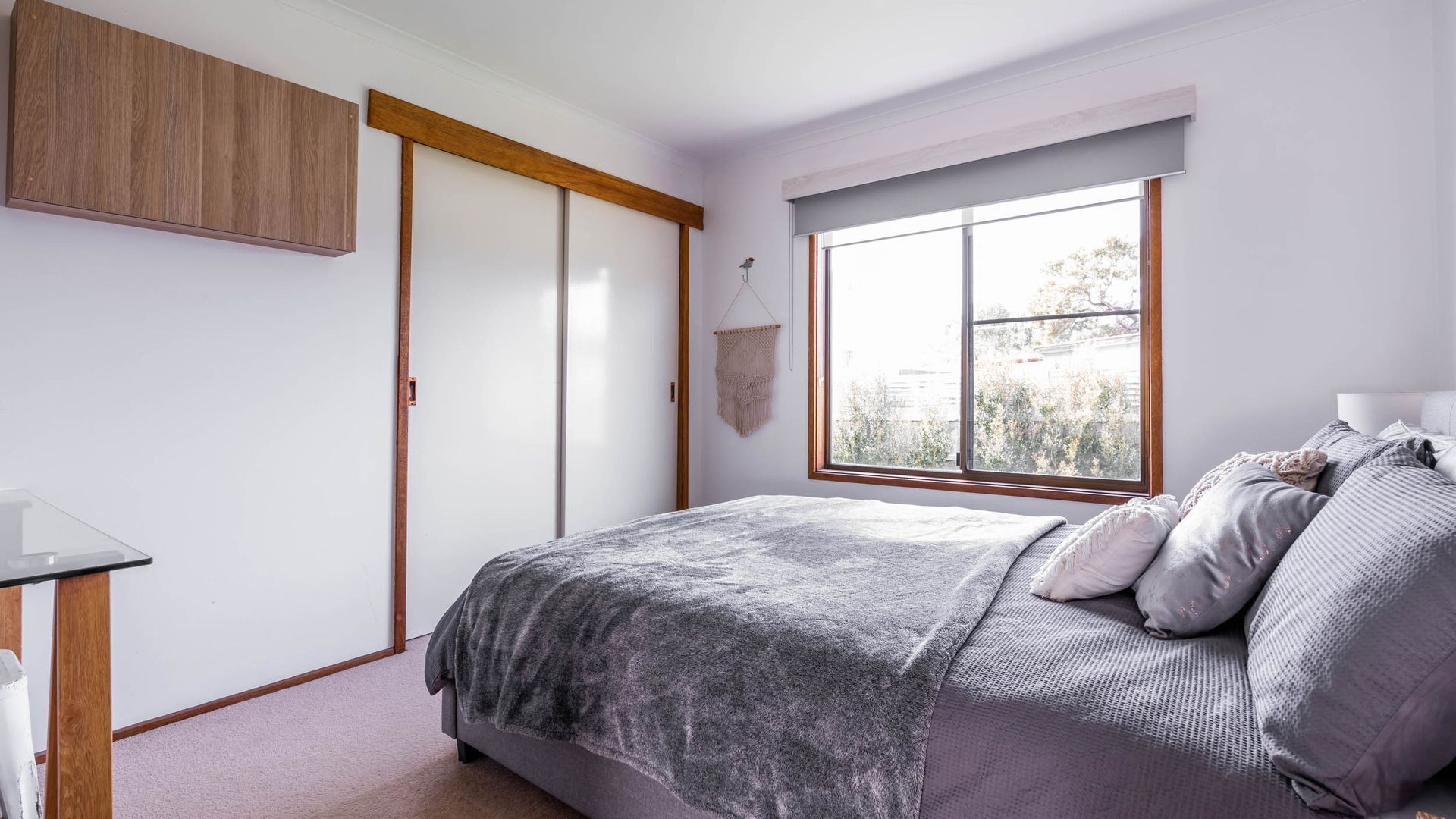 Een slaapkamer met een bed, een bureau, een kledingkast en een raam met uitzicht op bomen.