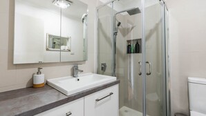 Un baño moderno con un lavamanos blanco, una cabina de ducha de vidrio y un espejo grande sobre el lavamanos.