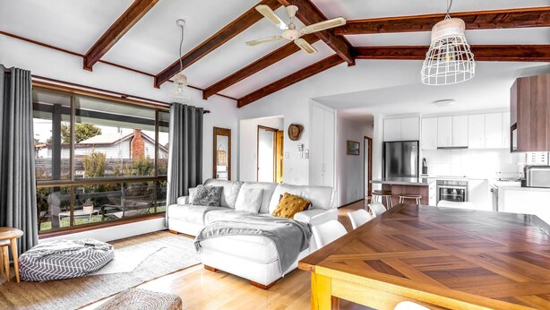 Una sala de estar moderna con un ventanal grande, techo de madera, un sofá y un comedor.