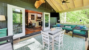 A rustic cabin interior with a dining area, a green sofa, and a mounted deer head. - Creekside Cabin: Tubing, Trails & Highlands Charm! (Highlands)