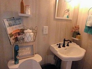 Ein Badezimmer mit weißem Waschbecken, Toilette, einem gerahmten Bild an der Wand und einer kleinen Ablage mit Pflegeprodukten.