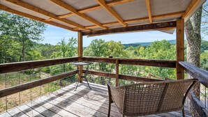 Un terrazzo in legno con tavolo e sedia, affacciato su un paesaggio boschivo.