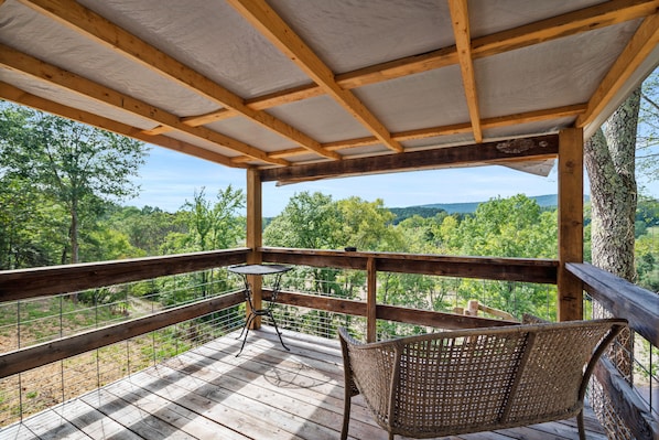 Une terrasse en bois avec une table et une chaise, donnant sur un paysage boisé.