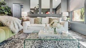 Een moderne woonkamer met een witte bank, een glazen salontafel en een grote spiegel boven de bank.