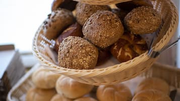En korg i flera våningar, fylld med olika sorters bröd, inklusive frallor och bullar, placerad på ett bord med en skylt som visar texten "ROSTAT BRÖD".