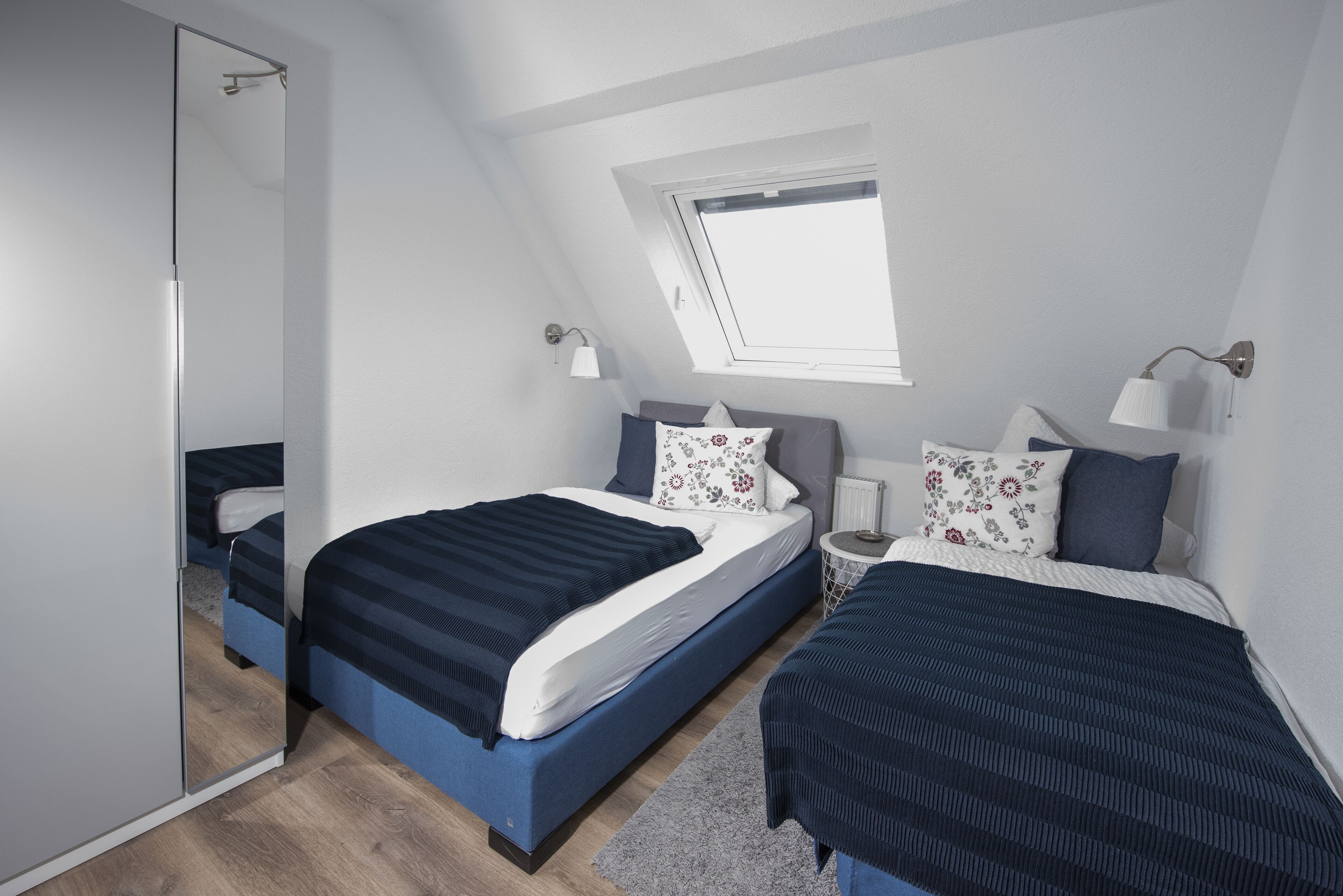 A bedroom with two beds, a skylight, and a mirror.