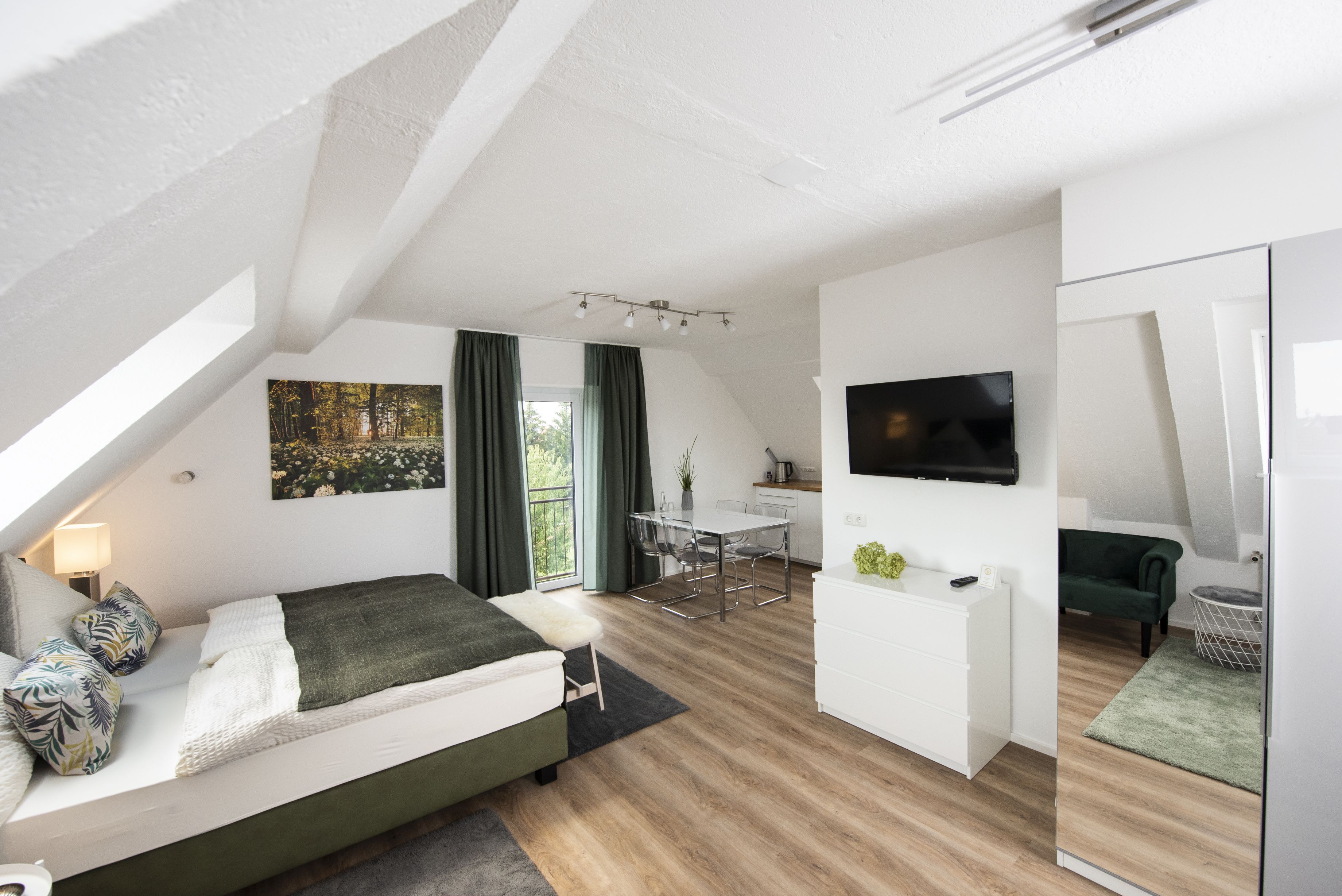 Una stanza moderna e luminosa con un letto, un'area pranzo, una TV e un divano verde.