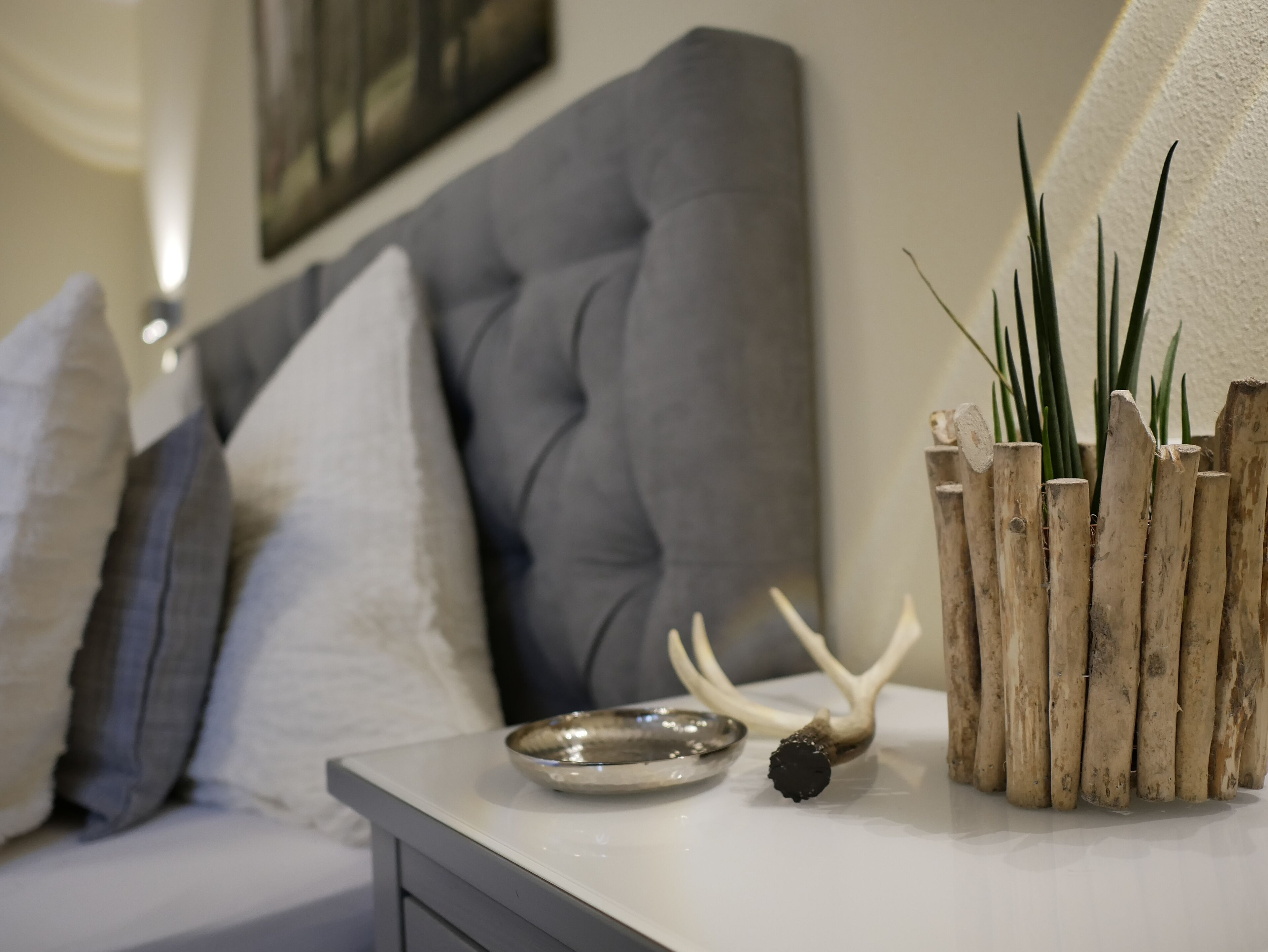 Un salon moderne avec un canapé gris, une petite table agrémentée d’objets décoratifs et un tableau accroché au mur.