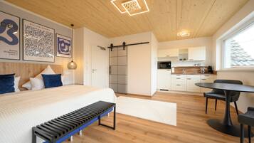 Ein modernes Schlafzimmer mit einem großen Bett, einer Bank, einer Schiebetür zu einer Küche und einem Essbereich mit Tisch und Stühlen.