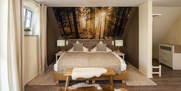 A bedroom with a large forest mural, a bed with a wooden headboard, bedside tables with lamps, and a small bench.