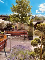 An outdoor seating area with wooden benches, a pergola, and a variety of potted plants and flowers.