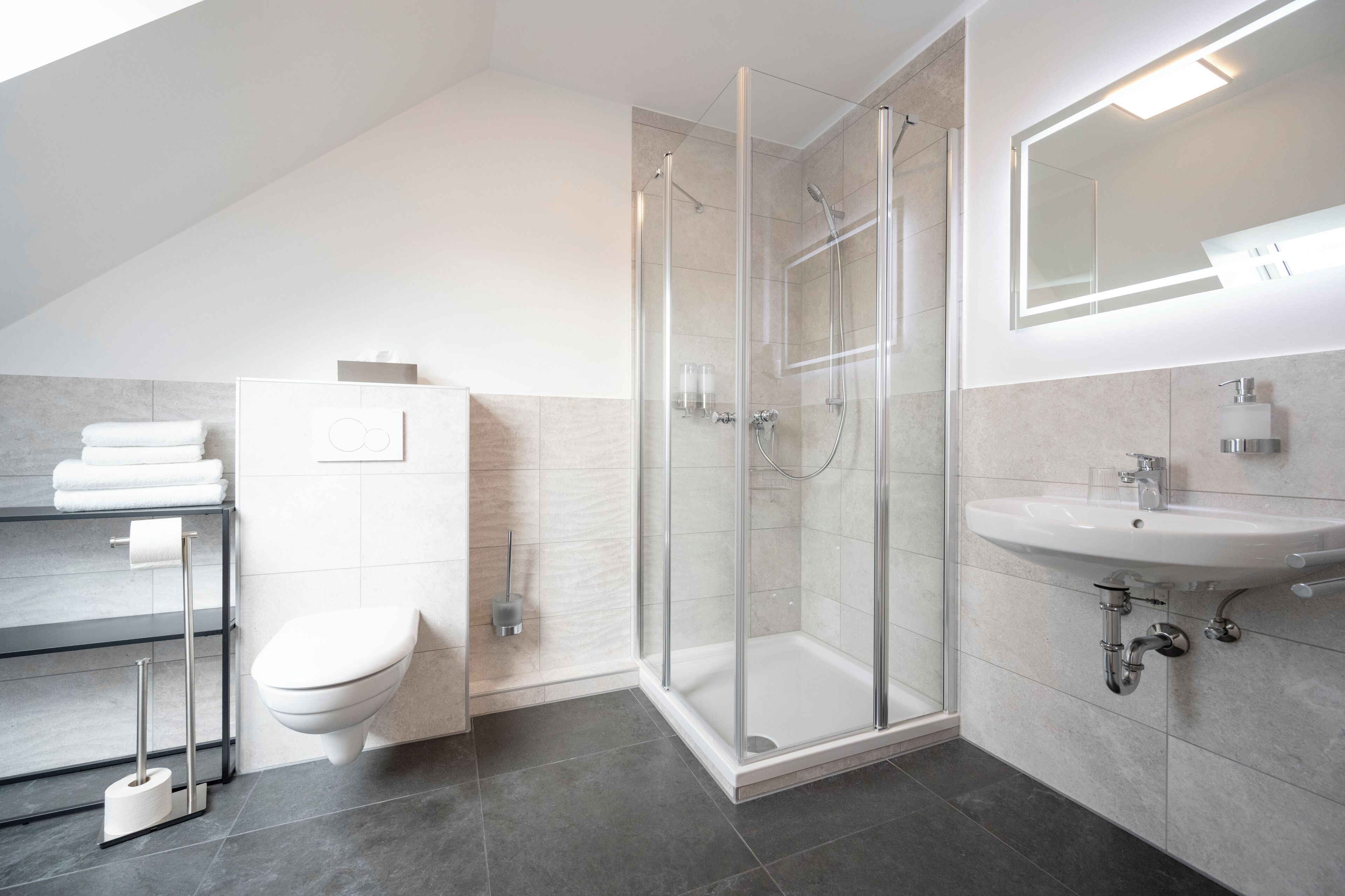 Een moderne badkamer met een glazen douchecabine, een wit toilet en een wastafel met een spiegel erboven.