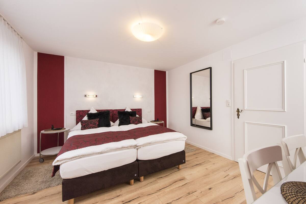 Ein modernes Schlafzimmer mit einem großen Bett, einem Nachttisch, einem Spiegel und einer Tür.