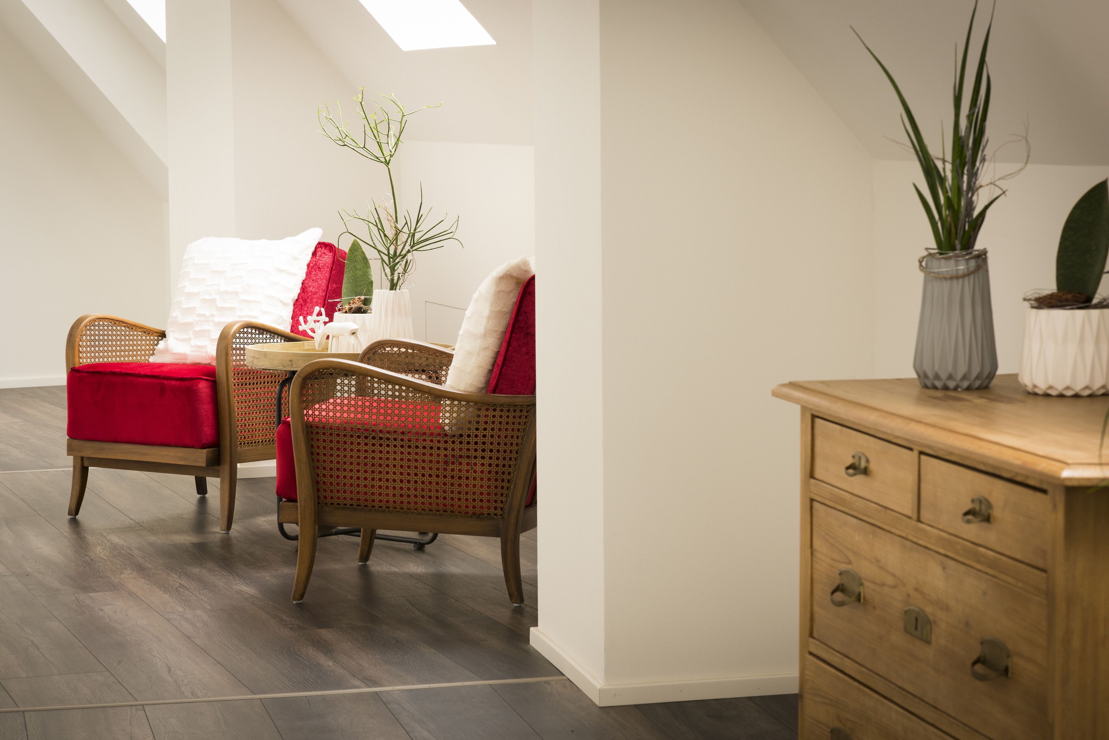 A room with two wicker chairs, a wooden dresser, and a plant.