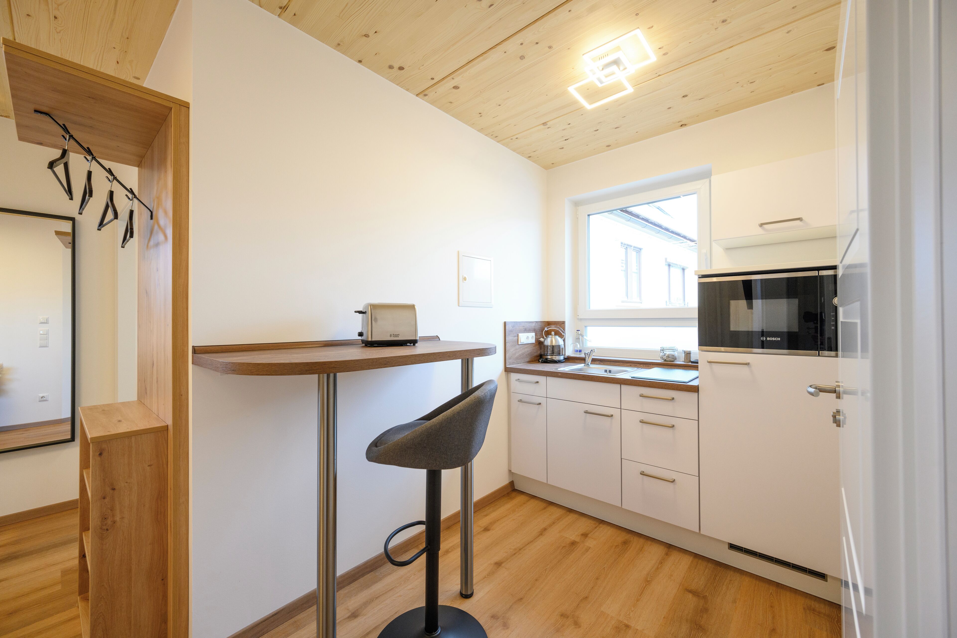 A modern kitchen with white cabinets, a Bosch microwave, and a bar stool.