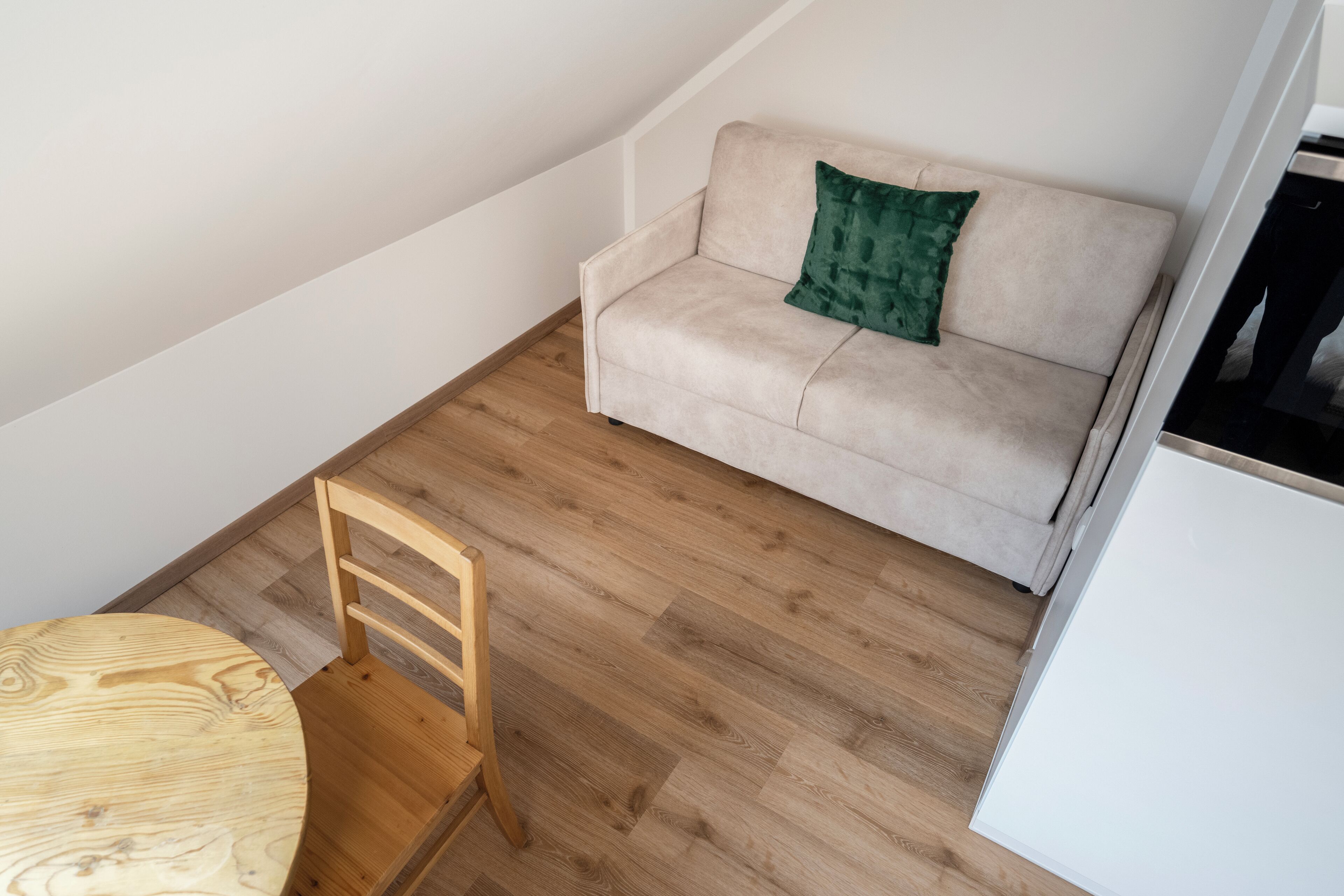 A room with a wooden dining table, a beige sofa with a green pillow, and a white cabinet.