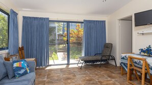 Ein Zimmer mit einer Couch, einem Sessel, einem Tisch mit einer Vase und einem Fernseher an der Wand.