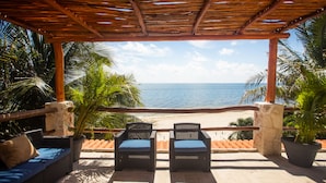 Un espace extérieur aménagé, abrité et doté de deux fauteuils en osier et d’un canapé, offrant une vue sur une plage et l’océan.