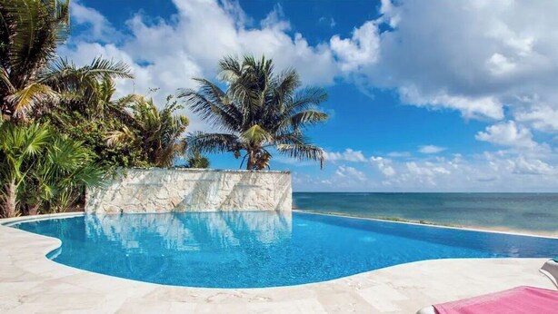 Une piscine bordée d’un mur de pierre et entourée de palmiers, avec vue sur une plage.