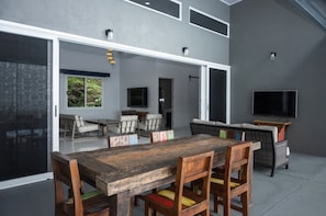 A spacious living area with a large wooden table and chairs, a sofa, and a television. - 5 Bedrooms, large pool & spectacular whale tail ocean view! (Uvita)