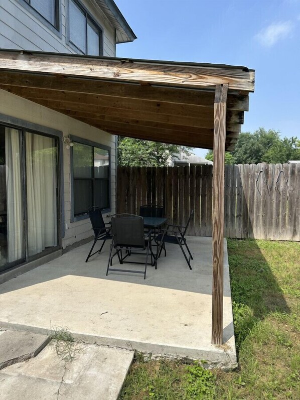 Un patio cubierto con una mesa, sillas, una pérgola de madera y suelo de hormigón.